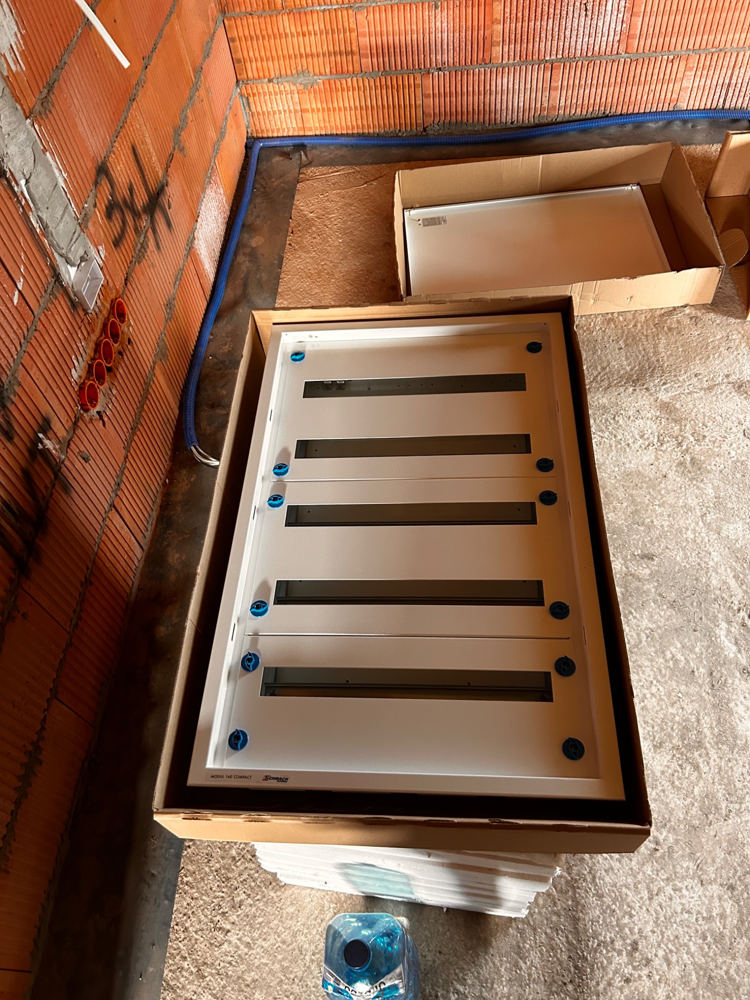 Rozdzielnica elektryczna w kartonie na budowie, widoczne przewody w ścianie z cegły. Przygotowanie do montażu instalacji w nowym budynku.