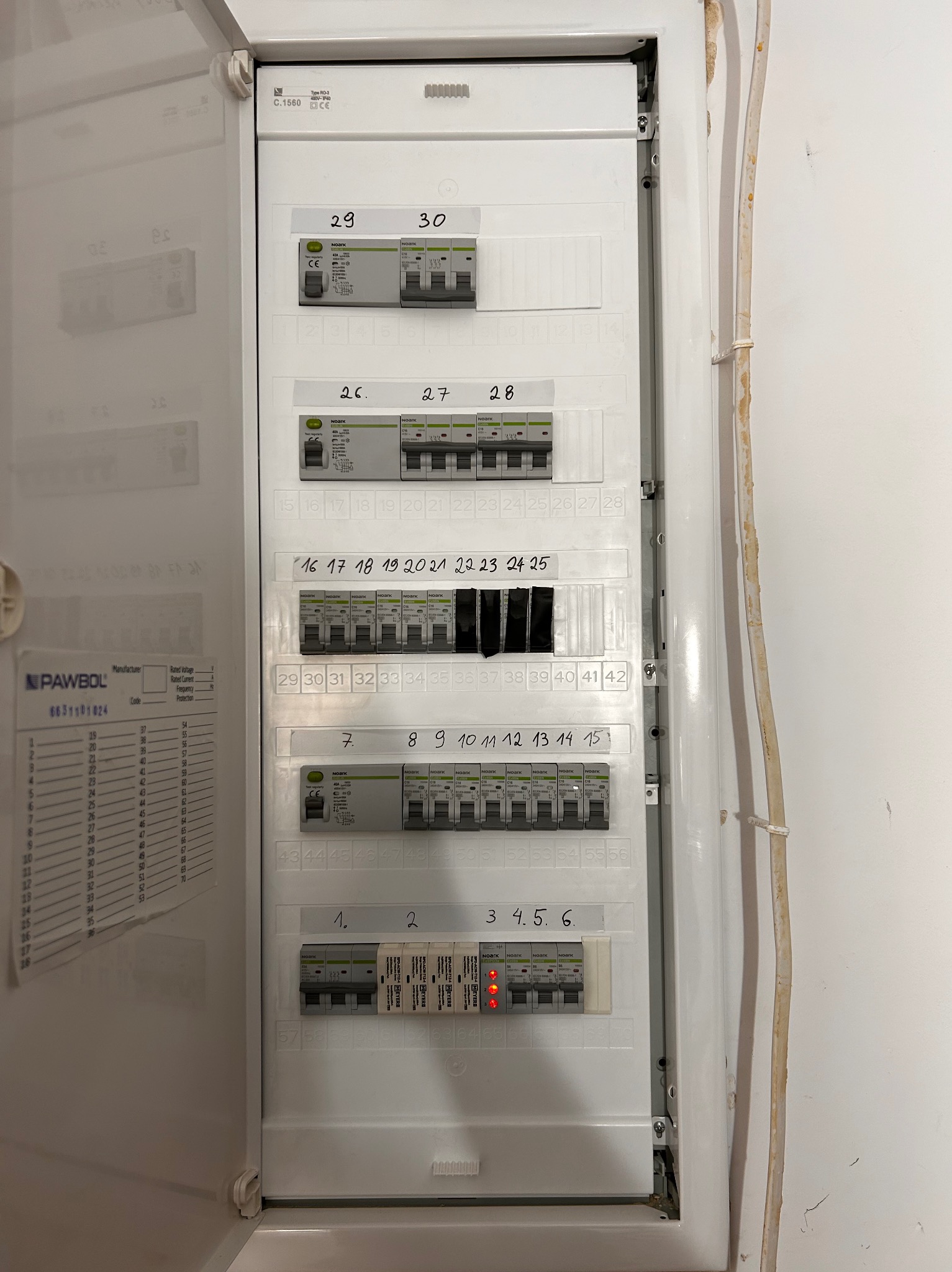 Otwarta skrzynka bezpiecznikowa z numerowanymi wyłącznikami, widoczne oznaczenia i specyfikacje techniczne. Jeden z wyłączników oznaczony numerami 3, 4, 5, 6 ma włączony czerwony wskaźnik.