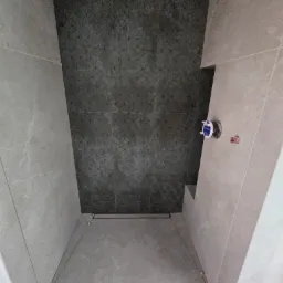 Wnętrze kabiny prysznicowej w trakcie układania płytek; na podłodze widoczne krzyżyki dystansowe, na ścianie ciemna mozaika kontrastująca z jasnymi płytkami.