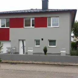 Dwukondygnacyjny dom z szarą elewacją i bordowymi akcentami, białe okna i drzwi, minimalistyczny ogródek przed domem, pochmurne niebo.