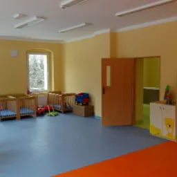 Jasne, przestronne wnętrze nowo wykończonego pokoju dziecięcego z żółtymi ścianami, niebieską podłogą, drewnianymi łóżeczkami, zabawkami i szafkami z motywami dziecięcymi.