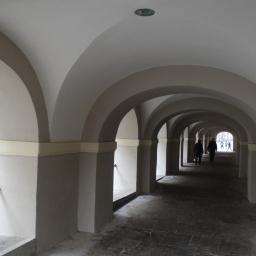 OLIWIA - Podcienia w Nowej Rudzie z rzędem łuków pomalowanych na szaro-biało, widok w głąb tunelu z przechodzącymi osobami.