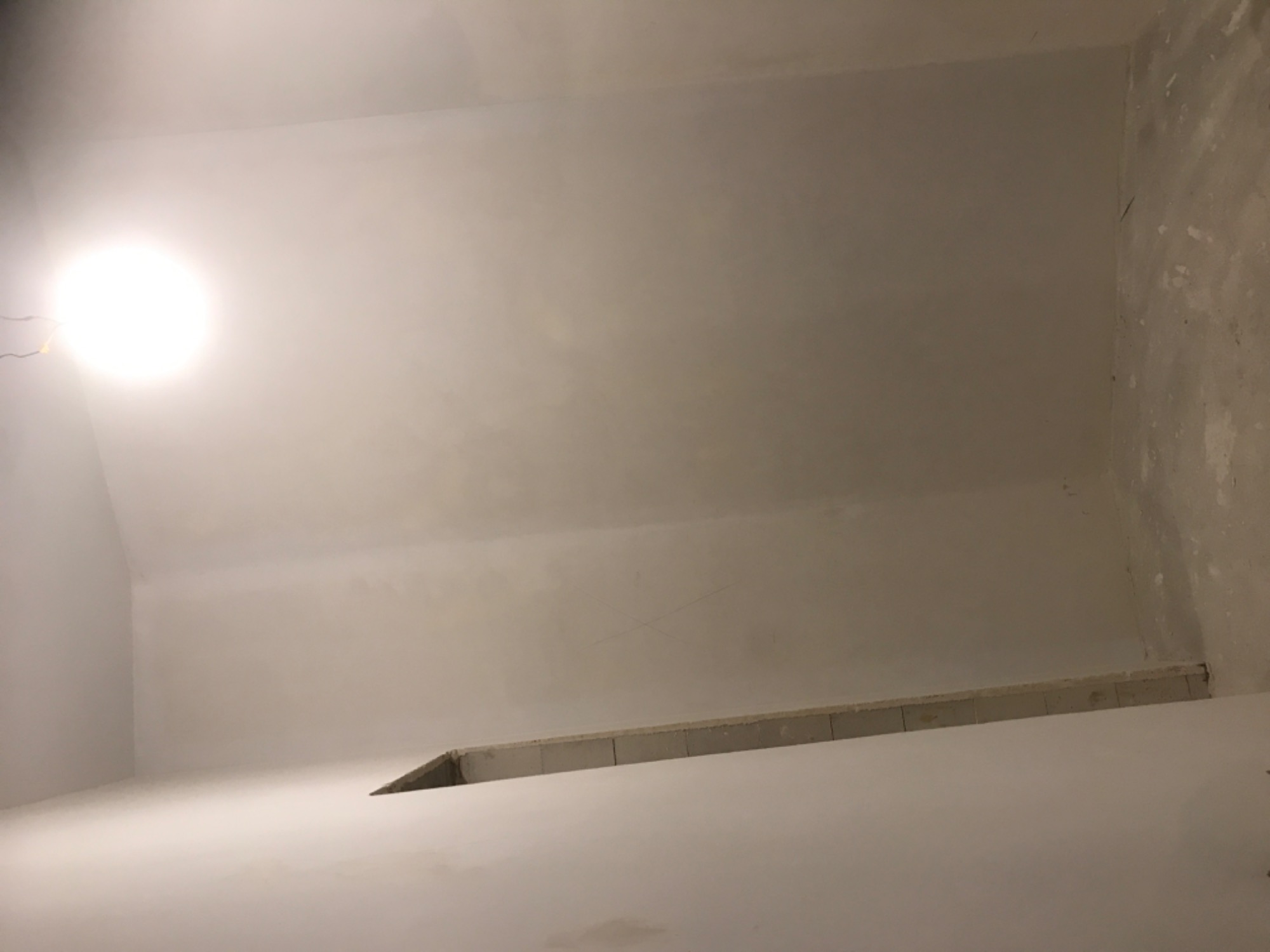 Świeżo otynkowane, białe ściany wewnętrzne pomieszczenia z widoczną instalacją podtynkową i punktowym oświetleniem sufitowym.