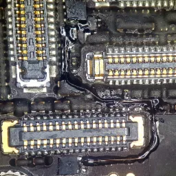 Zbliżenie na płytę główną telefonu po zalaniu, widoczne złącza pokryte topnikiem i ślady korozji.