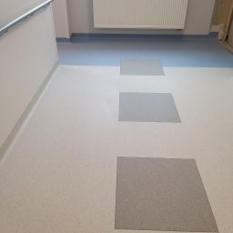 FLOOR-POL - Nowa podłoga z szarej i kremowej gumy w korytarzu, z szarą listwą przypodłogową i grzejnikiem ściennym.
