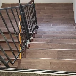 Schody wyłożone panelami imitującymi drewno, z czarną metalową balustradą i białymi ścianami, widok z góry.