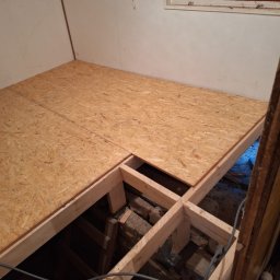 FLOOR-POL - Płyty OSB układane na drewnianej konstrukcji podłogi w pomieszczeniu z oknem z okiennicami.