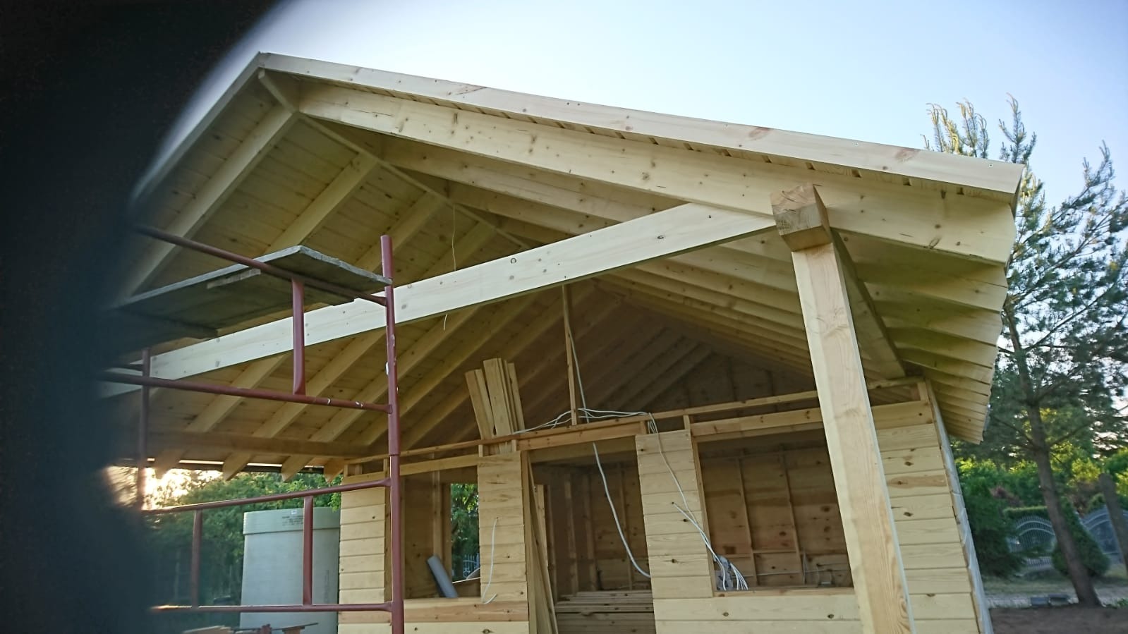 Surowa konstrukcja szkieletowa domu z widoczną więźbą dachową, rusztowaniem i instalacją elektryczną wewnątrz, w trakcie budowy.