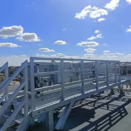 Instalacja rekuperacji na dachu budynku komercyjnego, widoczne metalowe schody i urządzenia, słoneczny dzień.