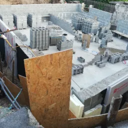 Wykop pod budynek z częściowo wzniesionymi ścianami fundamentowymi z bloczków betonowych, zabezpieczonymi izolacją pionową i deskowaniem szalunkowym.