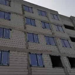 Wielopiętrowy budynek w trakcie budowy z częściowo zamontowanymi oknami, widoczne elementy konstrukcyjne i żuraw budowlany w tle.