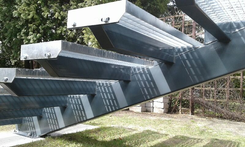 Metalowe schody zewnętrzne z kratownicowymi stopniami, zabezpieczone przed korozją, ustawione na trawniku w ogrodzie.