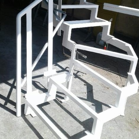 Szkielet stalowej konstrukcji schodów zabiegowych, pomalowany na biało, widoczny w surowym oświetleniu warsztatowym.