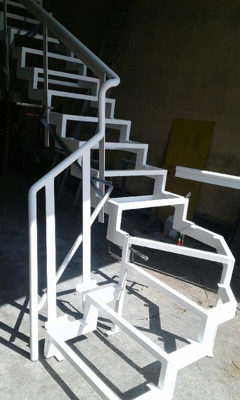 Szkielet białych, metalowych schodów z poręczą w warsztacie, widoczne spawane łączenia i surowe otoczenie.