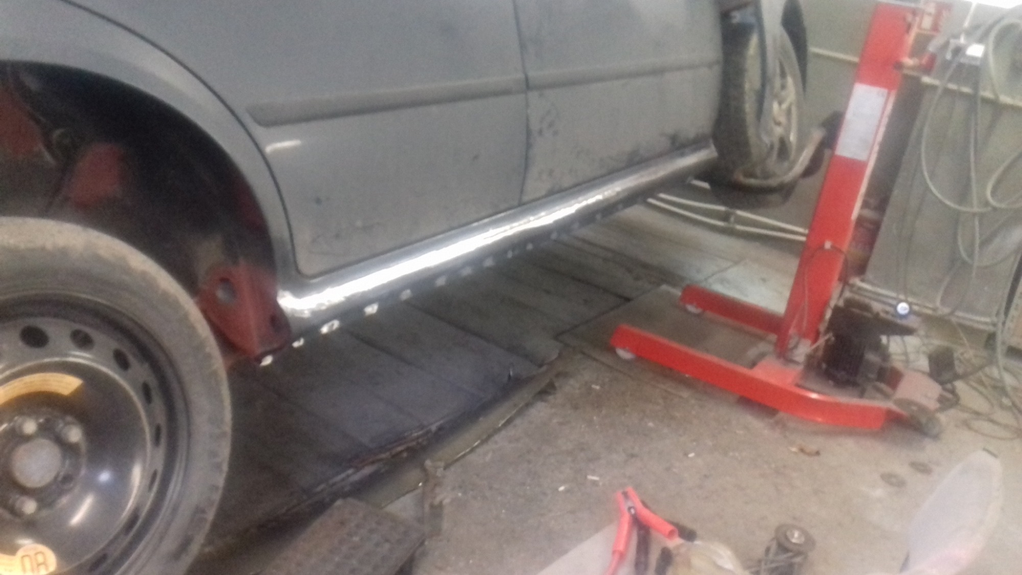 Szary samochód na podnośniku warsztatowym z zamontowanym nowym progiem, widoczne ślady spawania i niedomalowane fragmenty karoserii.