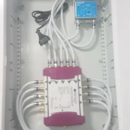 Wnętrze szafki z rozdzielaczem sygnału antenowego, widoczne kable koncentryczne z końcówkami, zasilacz i listwa zasilająca wewnątrz białej obudowy.