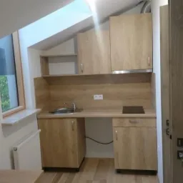 Mała, nowocześnie urządzona kuchnia w jasnych barwach z drewnianymi szafkami, z oknem na poddaszu i drewnianą podłogą.