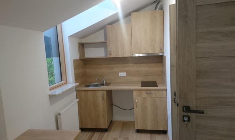 Mała, nowocześnie urządzona kuchnia w jasnych barwach z drewnianymi szafkami, z oknem na poddaszu i drewnianą podłogą.