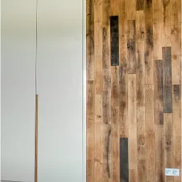 Biała szafa z drewnianymi uchwytami na tle ściany wyłożonej panelami z postarzanego drewna, z widocznymi gniazdkami elektrycznymi i dekoracją ze świec.