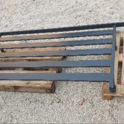 Element metalowego ogrodzenia panelowego w kolorze grafitowym, leżący na drewnianych paletach na tle żwirowego podłoża.