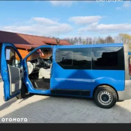 Niebieski bus z otwartymi drzwiami na tle budynku z brązowym dachem.