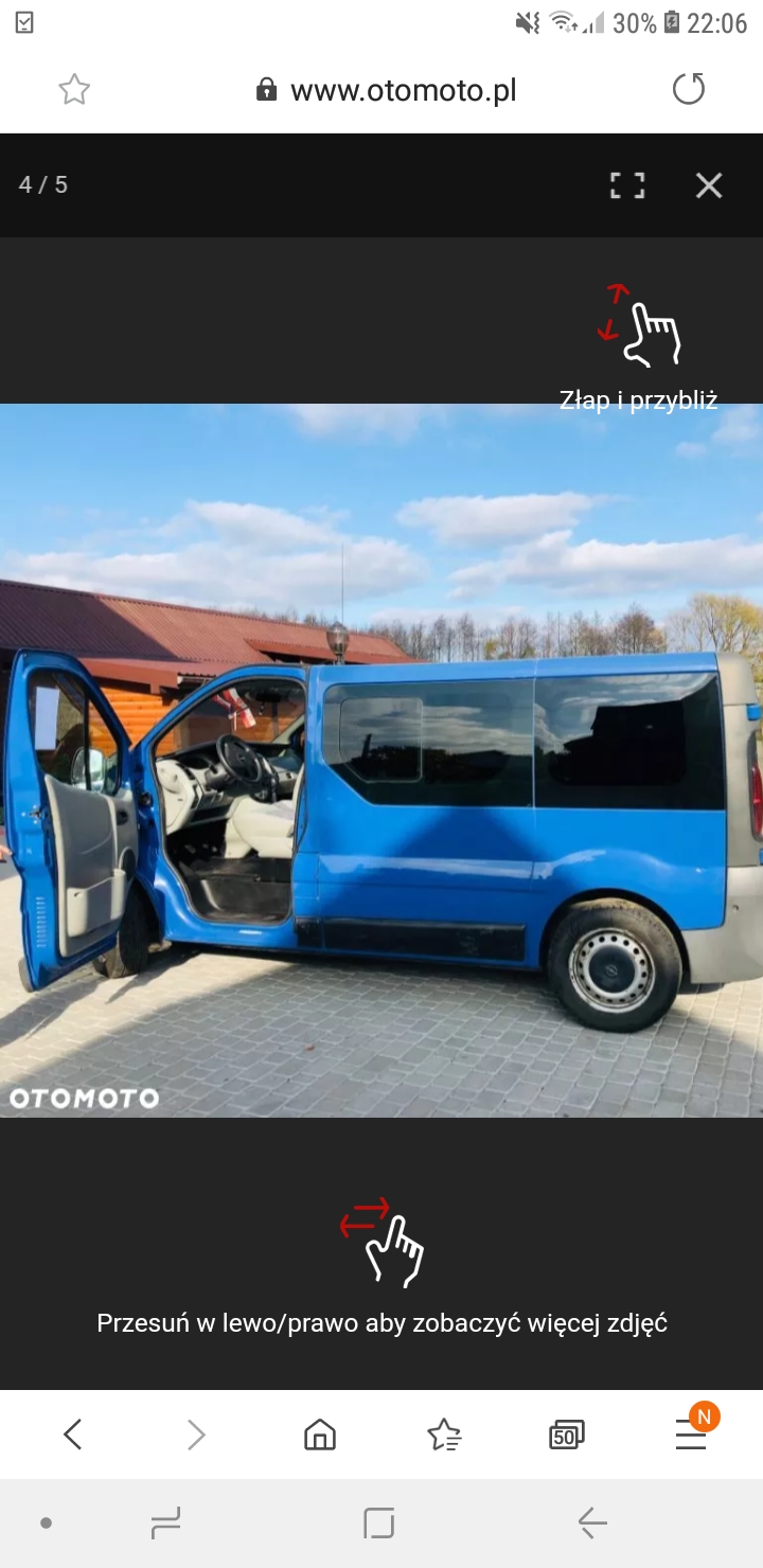 Niebieski bus z otwartymi drzwiami na tle budynku z brązowym dachem.
