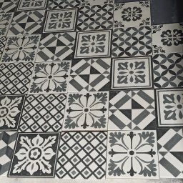 Usługi remontowe - wykończenia wnętrz Daniel Budner - Ułożone, wzorzyste, czarno-białe płytki podłogowe w łazience z widoczną ścianą w surowym stanie.