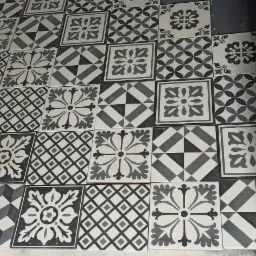 Ułożone, wzorzyste, czarno-białe płytki podłogowe w łazience z widoczną ścianą w surowym stanie.