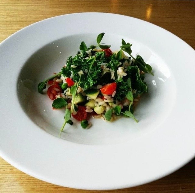 Apetyczna kompozycja: ryż z jarmużem, pomidorkami cherry, groszkiem i ziołami, podana na białym talerzu na drewnianym stole.