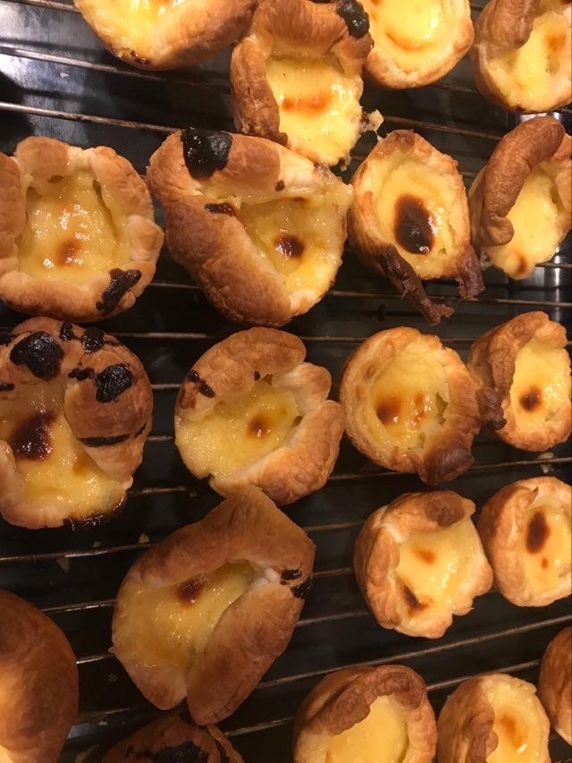 Tarty z kremem budyniowym na metalowej kratce, niektóre z lekko przypalonym wierzchem, ukazane z bliska.