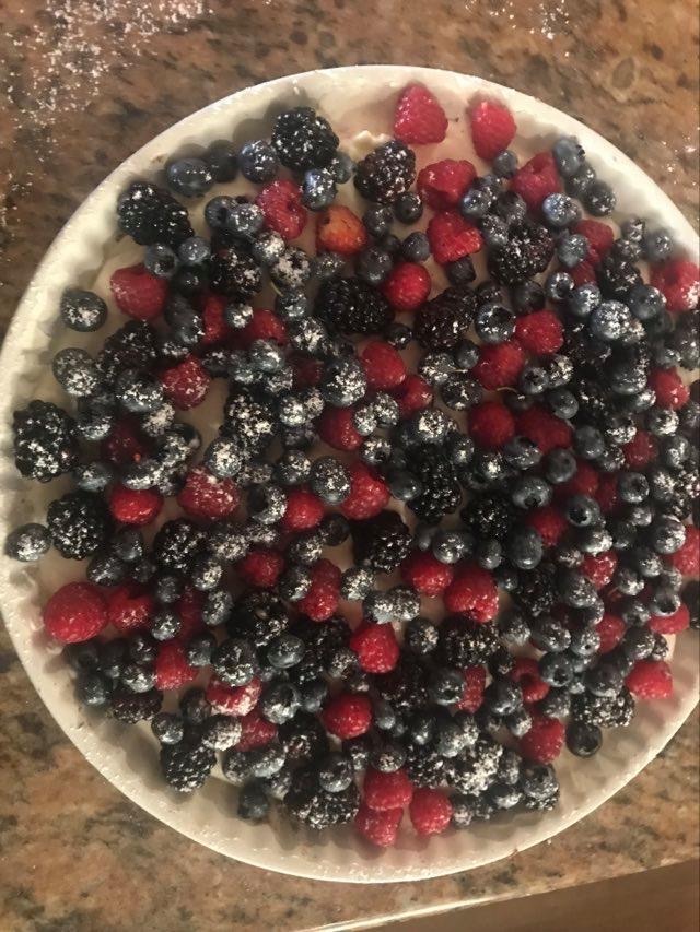 Tarta z owocami leśnymi posypana cukrem pudrem, widok z góry, na marmurowym blacie.