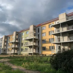 Nowoczesny budynek wielorodzinny z balkonami o stalowej konstrukcji, widoczne elementy ocynkowane, gotowe do montażu, fasada w odcieniach żółci i zieleni, na pierwszym planie zieleń.