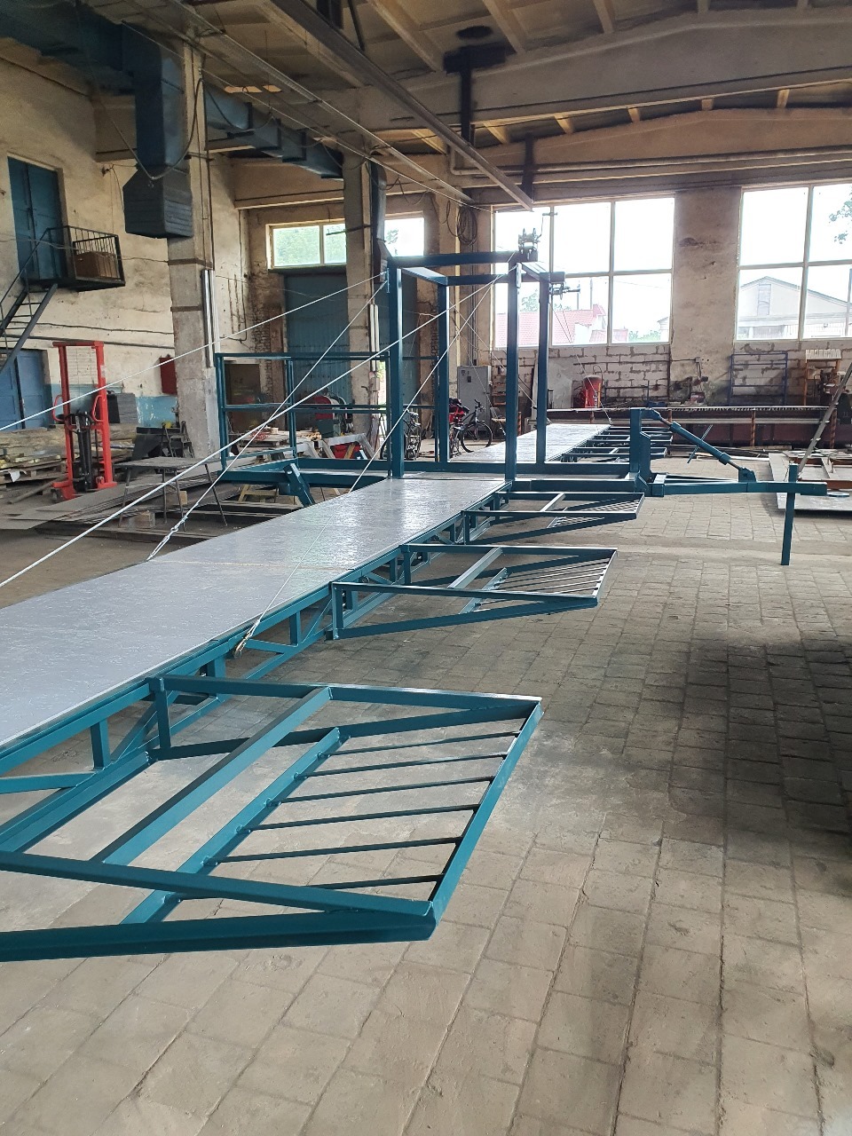 Wnętrze hali produkcyjnej z konstrukcją stalową pomalowaną na niebiesko, prawdopodobnie w trakcie montażu lub po spawaniu, widoczne okna i oświetlenie przemysłowe.