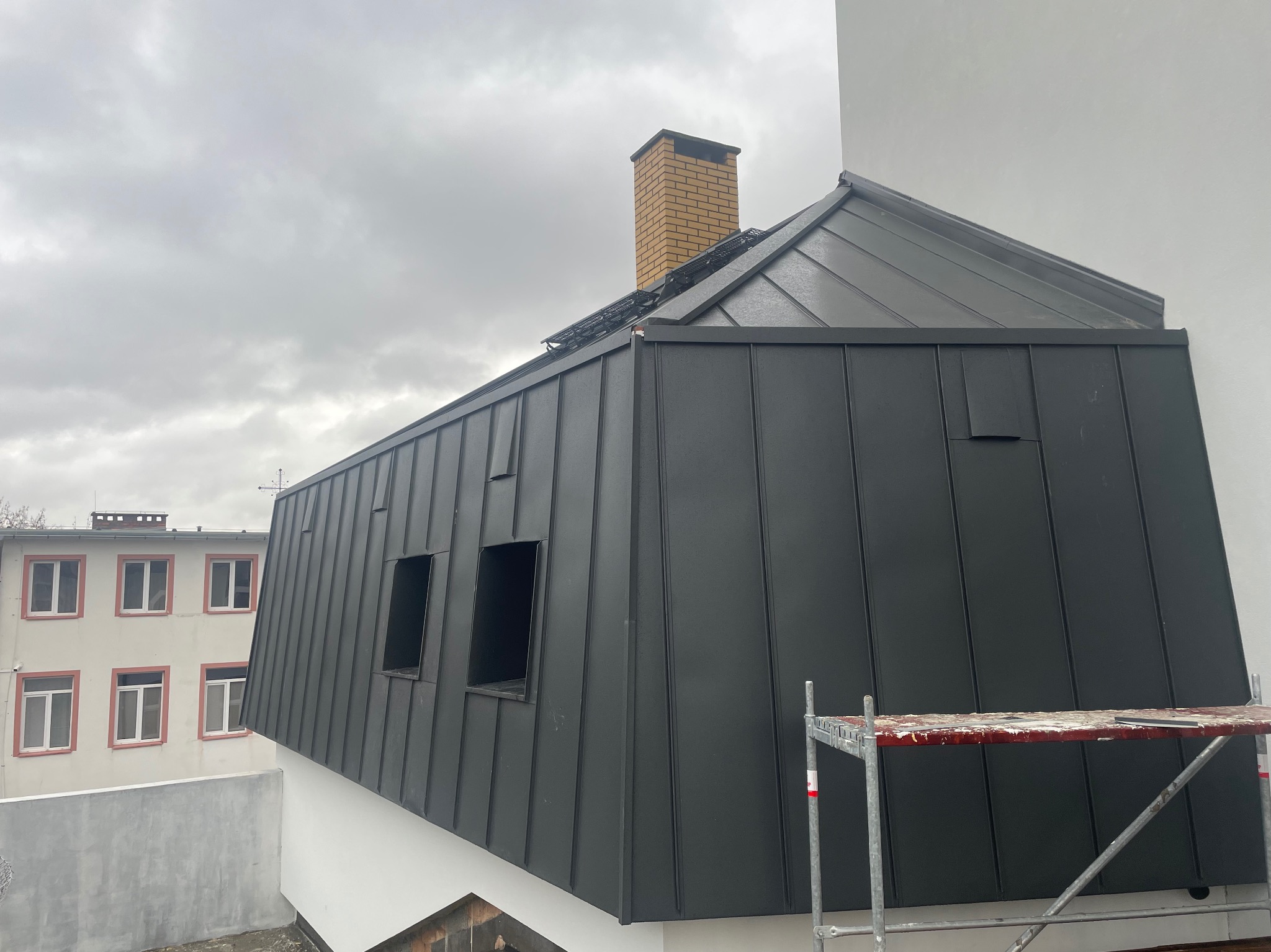 Nowoczesny dach z blachy na budynku z ceglanym kominem, widok z rusztowania, pochmurne niebo.