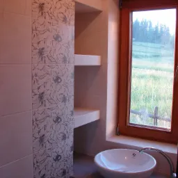 Jasna łazienka z umywalką nablatową, płytkami z motywem kwiatowym i widokiem na zieleń za oknem.