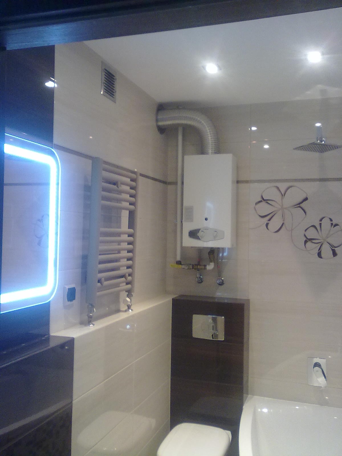 Nowoczesna łazienka z podświetlanym lustrem, grzejnikiem drabinkowym, zabudowaną spłuczką WC i piecem gazowym z odprowadzeniem spalin