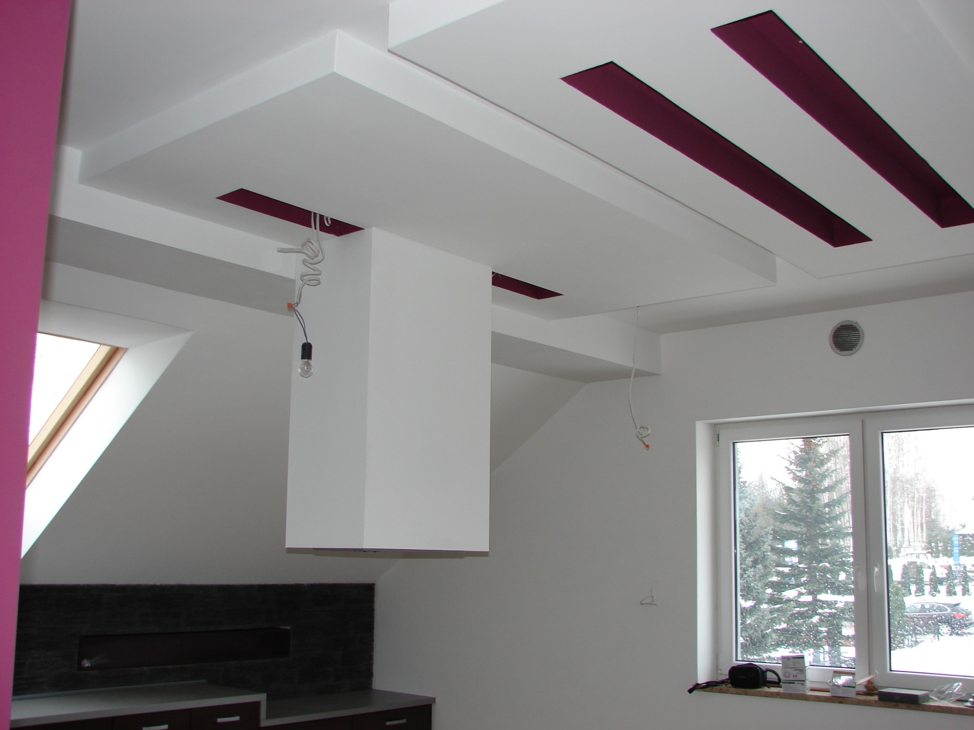 Wykończony sufit podwieszany z białymi panelami i purpurowymi wstawkami, widoczne niedokończone kable elektryczne, fragment okna z widokiem na zimowy krajobraz.