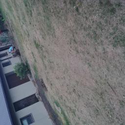 Zaklad-elektrobudowlany - Dwaj mężczyźni pracują w ogrodzie przy domu z szarą elewacją i brązowymi drzwiami, jeden grabi, drugi przewozi coś w taczce, widoczne róże przy ścianie budynku.