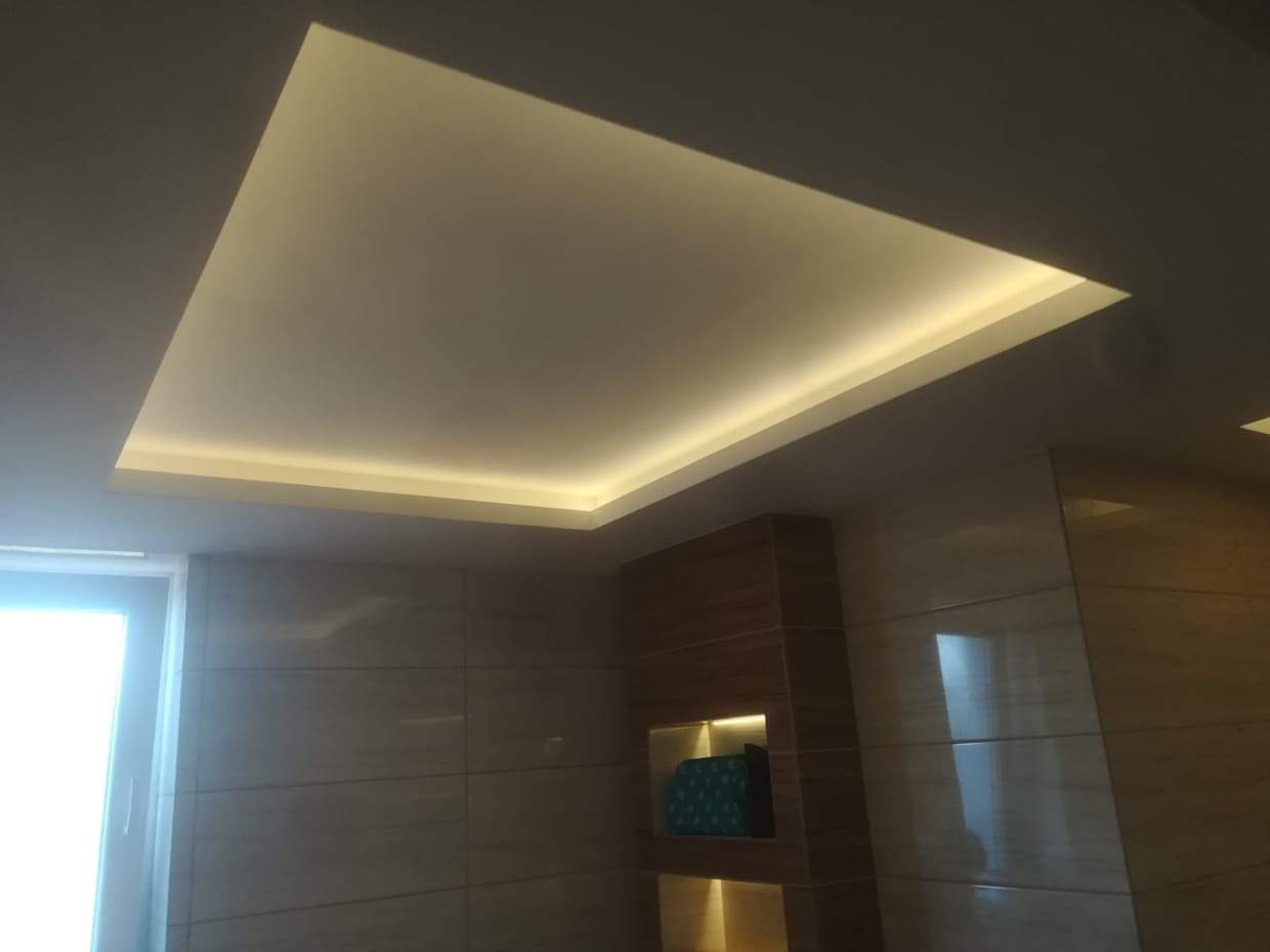 Podwieszany sufit z oświetleniem LED w nowoczesnym wnętrzu, widok z dołu, kremowe płytki na ścianach, drewniana wnęka dekoracyjna.