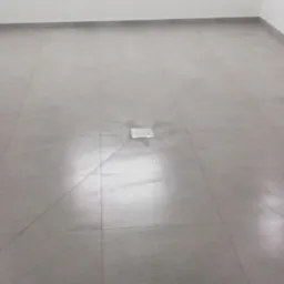 Świeżo ułożona, jasnoszara podłoga z płytek ceramicznych z centralnie umieszczonym odpływem podłogowym, widoczne linie fug krzyżujące się pod kątem.