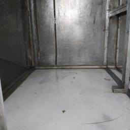 Hydraulik/Monter klimatyzacji - Wnętrze metalowej komory z białą podłogą, widoczne ślady użytkowania i konstrukcja wsporcza.