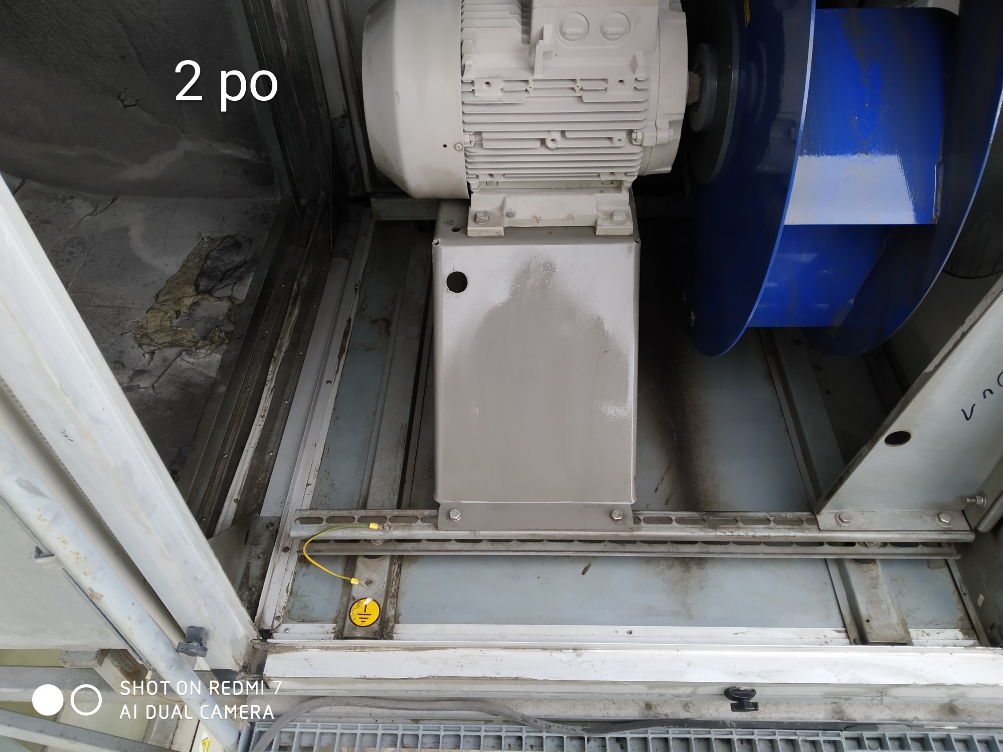 Wnętrze centrali wentylacyjnej z widocznym silnikiem, wentylatorem promieniowym i elementami instalacji elektrycznej, w tym uziemieniem.