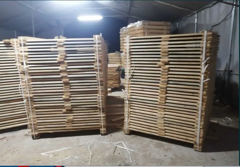 Stosy świeżo przetartej tarcicy budowlanej, zabezpieczone sznurkiem, składowane w hali oświetlonej lampą jarzeniową.