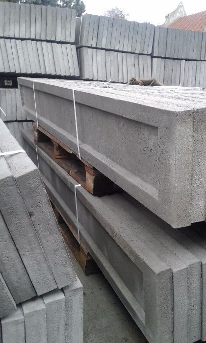 Prefabrykowane, szare elementy betonowe z charakterystycznym wgłębieniem, ułożone na drewnianych paletach i zabezpieczone białym sznurkiem, przygotowane do transportu lub montażu.