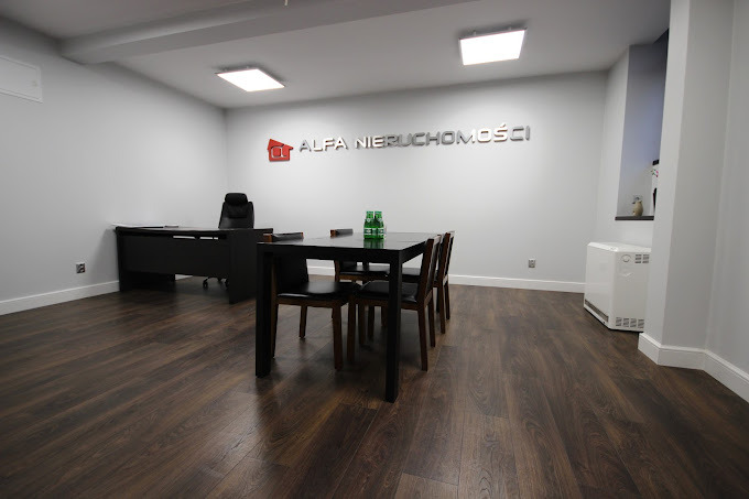 Nowoczesne biuro agencji nieruchomości z ciemną podłogą, czarnym biurkiem i stołem konferencyjnym, logo firmy na ścianie.