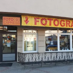 Fasada budynku Foto Express z szyldem 'Fotograf' i wystawą zdjęć w oknach.