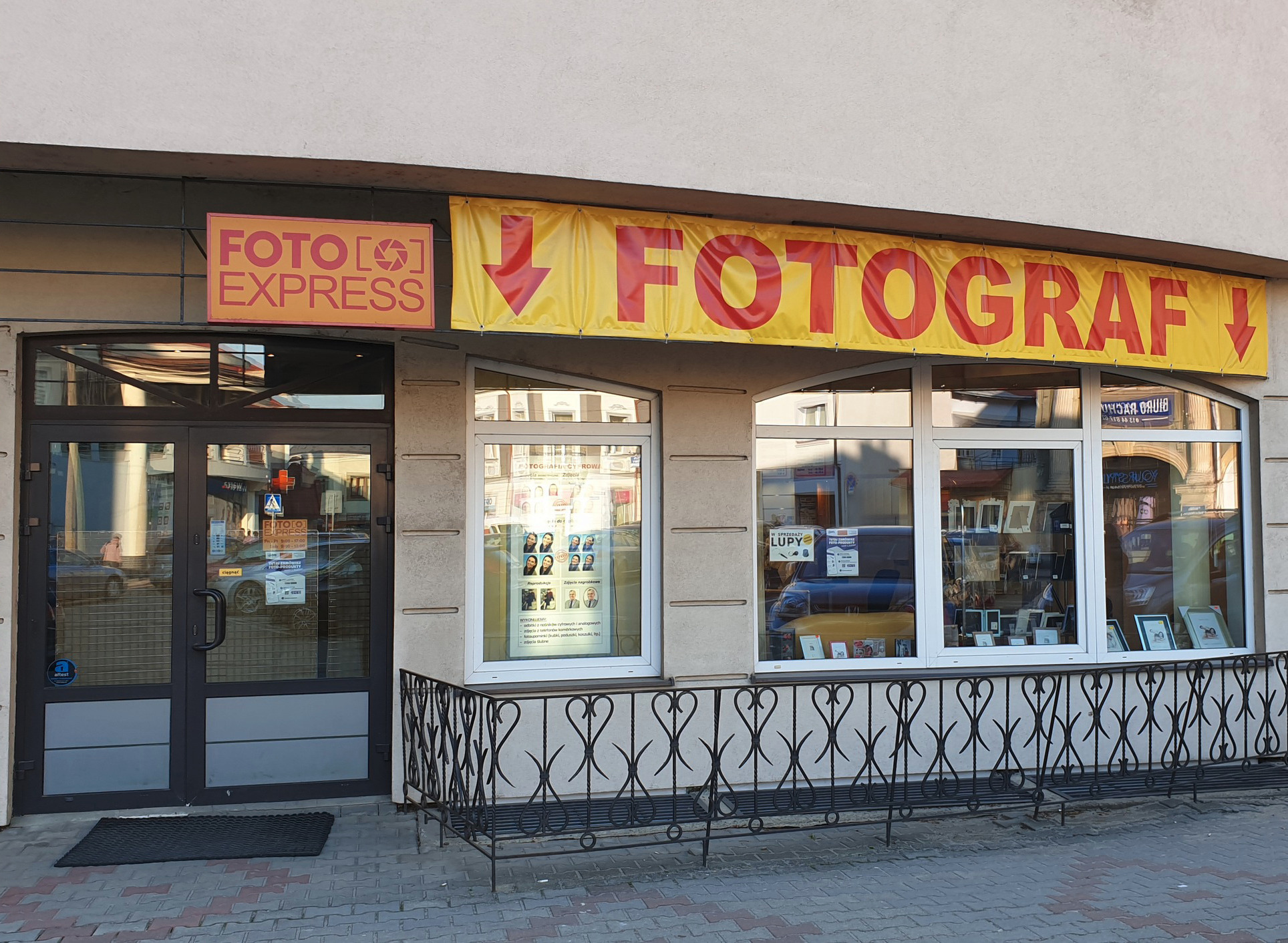 Fasada budynku Foto Express z szyldem 'Fotograf' i wystawą zdjęć w oknach.