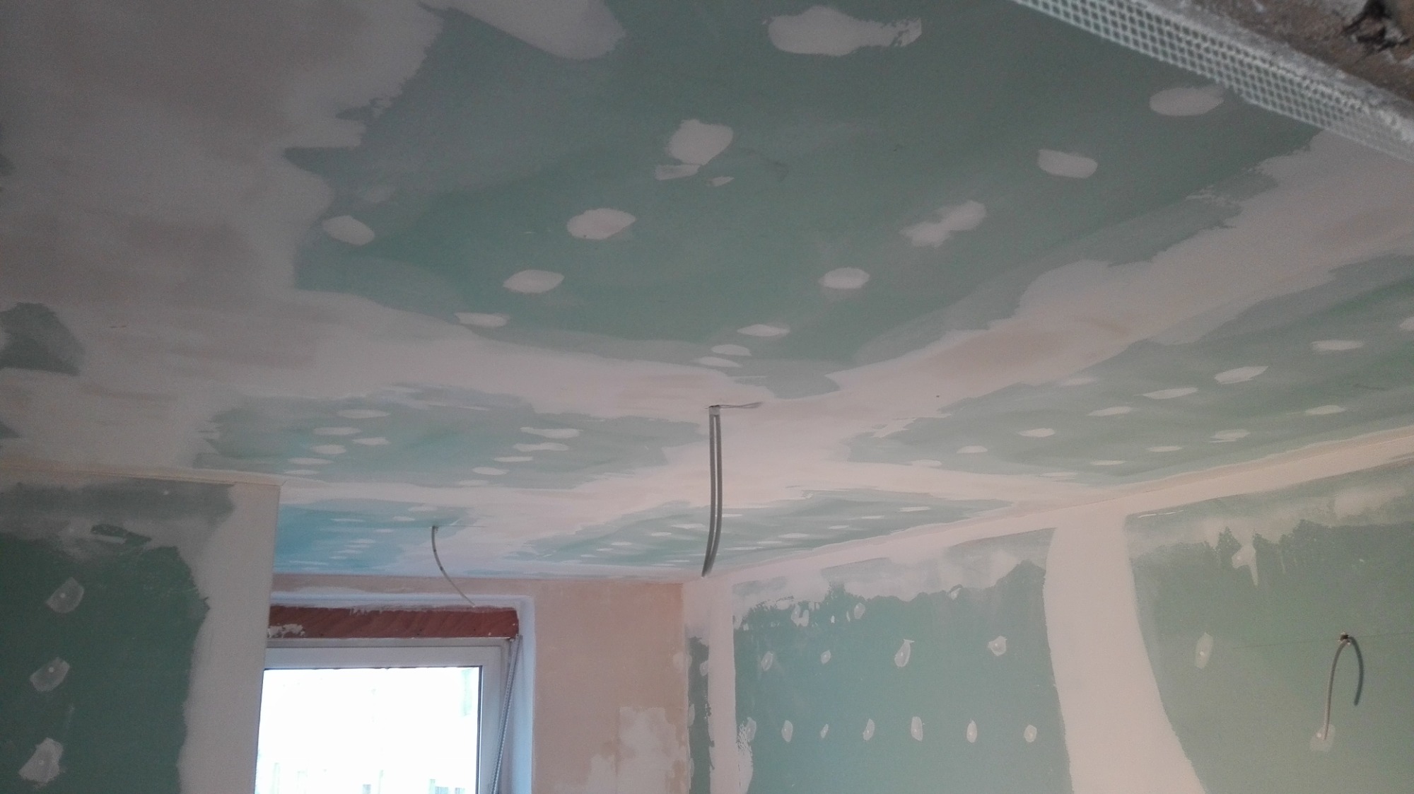 Sufit i ściany w trakcie prac wykończeniowych, widoczne ślady po szpachlowaniu i siatka narożna, przewody wystające z sufitu.