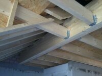 Konstrukcja drewniana dachu z widocznymi elementami mocującymi z metalu, płyty OSB w tle, ujęcie od dołu pod kątem.