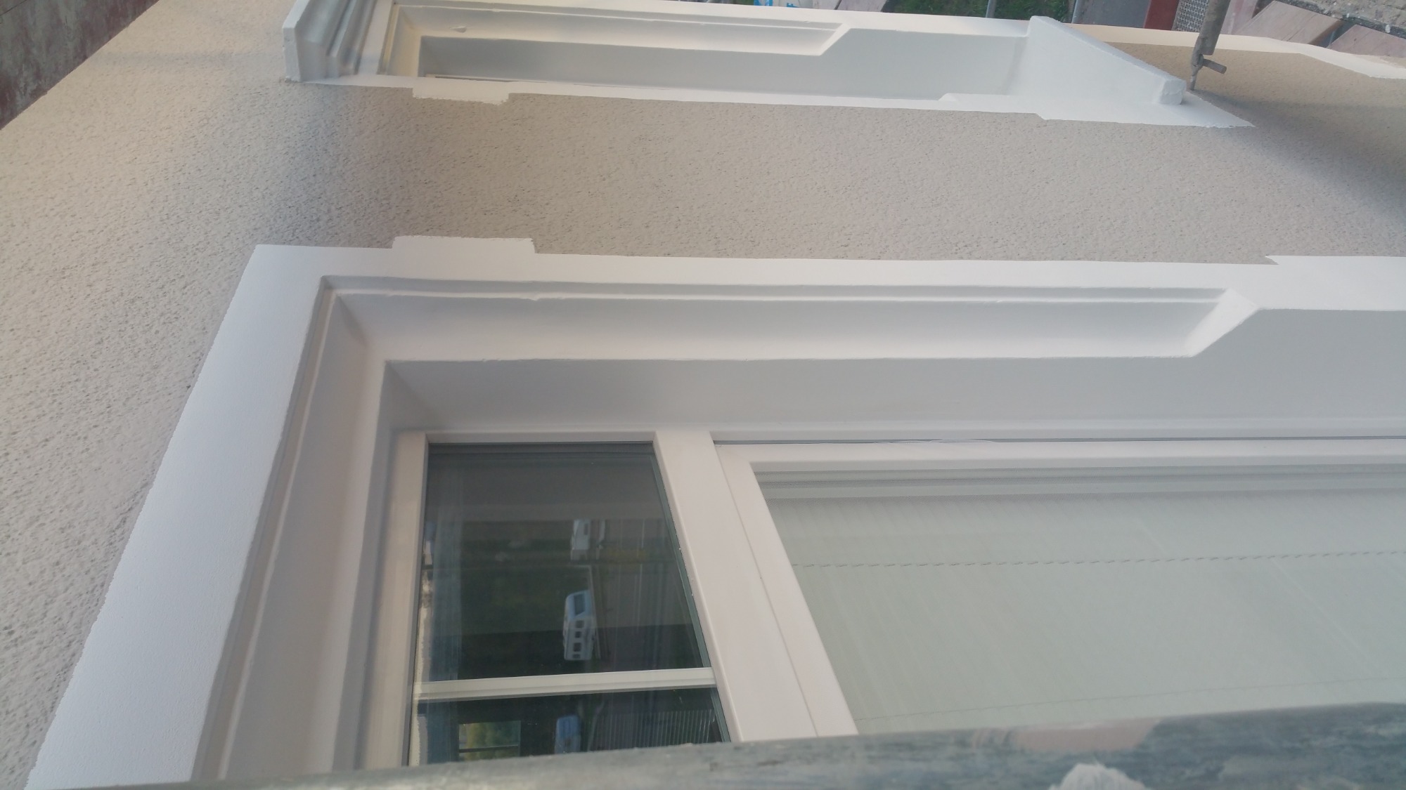 Wykończona elewacja domu z oknem w białej ramie i ozdobnymi listwami, widoczne detale struktury tynku baranka i świeżo pomalowane elementy